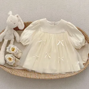 Flat lay of cream long-sleeve mesh dress with bow detail and lace baby shoes