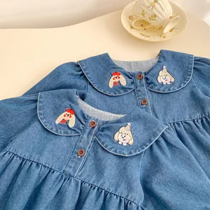 Detail shot of girls denim dress featuring cute cartoon embroidery on a wide doll collar