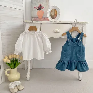 Close-up of baby girl denim heart overall dress with ruffled white long sleeve shirt