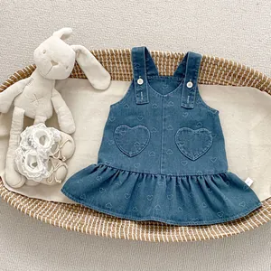 Detail of blue denim baby dress with heart embroidery and ruffled hem in a woven basket
