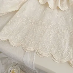 Dettaglio del ricamo floreale e dell'orlo in pizzo smerlato sulla camicia color crema