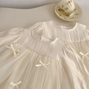 Detail of cream long-sleeve mesh dress with delicate bows and satin finish for girls