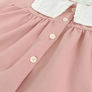 Detailed view of girls' pink blouse featuring a white lace collar and wooden buttons
