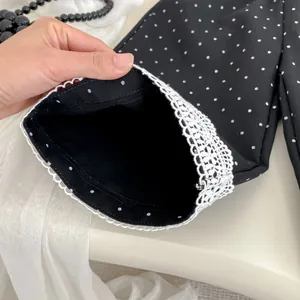 Dettaglio del tessuto a pois neri con bordo in pizzo bianco sui polsini