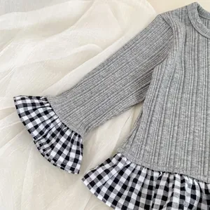 Detail van grijs gebreid vest met zwart-witte ruitjes aan de geplooide zoom voor meisjes