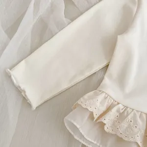 Detail of cream-colored girl's knit top featuring intricate eyelet lace embroidery hem