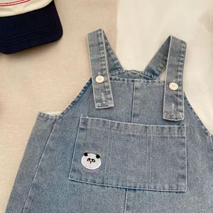 Dettaglio della salopette in denim azzurro per neonato con ricamo panda e bottoni bianchi
