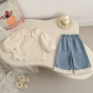 Dettaglio di un top in pizzo bianco e pantaloni in denim con volant per bambine piccole