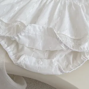 Close-up of white baby bodysuit with layered ruffles, lace trim and bottom snap buttons