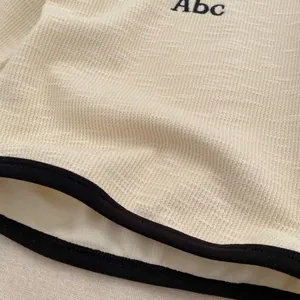 Detail of cream waffle knit fabric with black embroidered Abc text on a toddler boy shirt