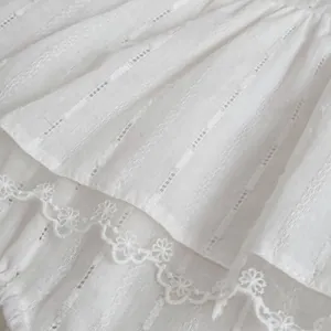 Detailed close-up of white floral lace embroidery and pleated cotton fabric on baby romper