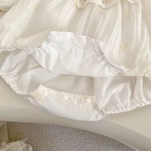 Detail eines Baby-Stramplers mit Spitzenbesatz, Blumenstickerei und Druckknöpfen