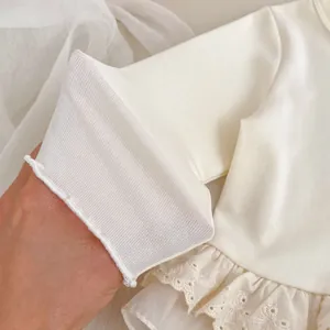 Detailed macro of white ribbed cotton baby top with delicate lace and embroidery