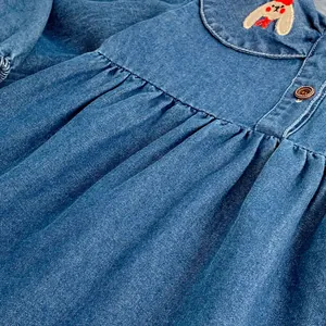 Close-up of cute cartoon rabbit embroidery on girl's denim dress with wooden buttons