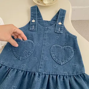 Girls denim overall dress with heart embroidery and button straps on cream background