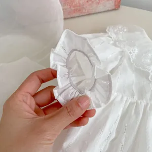 Detail of white cotton baby romper featuring ruffle cuffs and delicate lace neckline