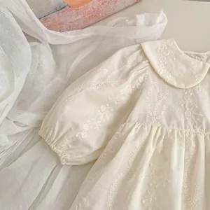 Dettaglio del ricamo floreale sulla tutina da neonata color crema con maniche a sbuffo