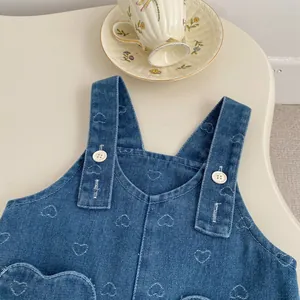 Detail of toddler denim pinafore dress with white heart embroidery and button straps