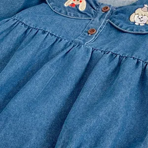 Detail of dog embroidery and wooden buttons on girls' denim dress Peter Pan collar