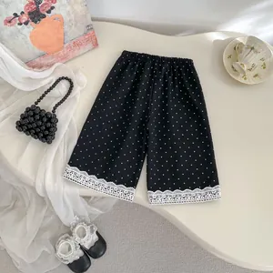 Vista piatta di pantaloncini neri a pois per bambina con bordo in pizzo bianco pregiato