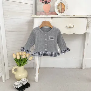Detail van grijs gebreid vest met gingham ruches en kanten patch op de voorkant van de top