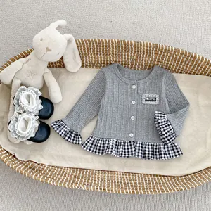 Detail van grijs gebreid babyvest met geruite ruches aan de zoom en witte knopen