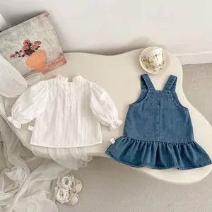 Flat lay of girl's white ruffle shirt and blue heart print denim overall dress set