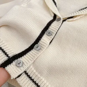 Close-up of knit cardigan with black trim, textured fabric, and grey marbled buttons