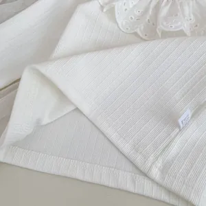 Detalle de camiseta de punto blanco para niña con cuello de encaje y textura acanalada