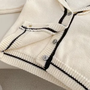 Detailed macro view of cream knitted cardigan with black contrast trim and buttons