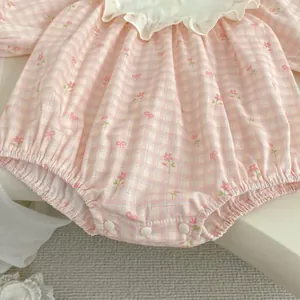 Dettaglio di pagliaccetto rosa a quadretti con motivi floreali e colletto a balze