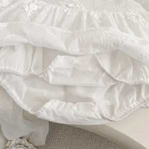Detail of white baby bodysuit with floral embroidery and snap button closure