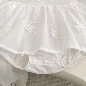 Detail of baby girl's white cotton bodysuit dress with floral embroidery and snap buttons