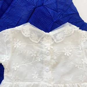 Close-up of white baby girl romper featuring floral embroidery and lace doll collar