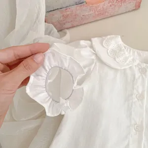 Dettaglio di camicia bianca per neonata con colletto ricamato e polsini con volant