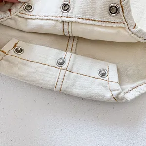 Detail of metal snap fasteners and brown stitching on baby denim romper fabric