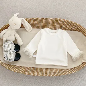 Detalle de camiseta de bebé crema de manga larga con puños de encaje y zapatos negros