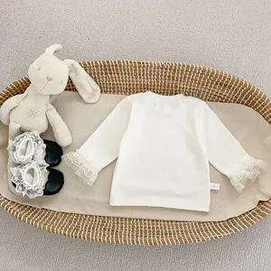 Detalle de camiseta blanca de manga larga para bebé con puños de encaje en cesta
