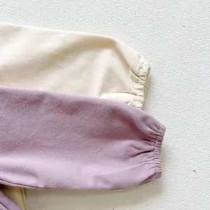 Close-up of elastic ribbed cuffs on cream and lilac cotton baby bodysuits with soft texture