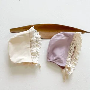 Close-up of baby lace bonnets in cream and purple with fine embroidery and ties