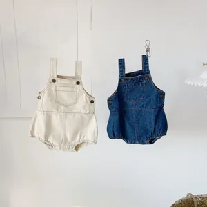 Baby denim overalls in cream and navy blue cotton, hanging against a white wall