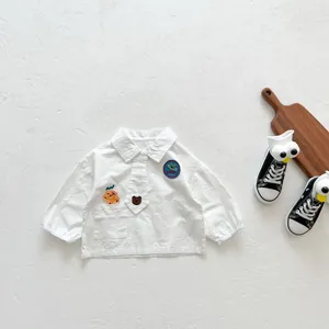 Détail d'une chemise bébé en coton blanc avec broderie ours et badge décoratif sur la poitrine