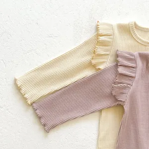Close-up of ribbed cotton baby onesies with ruffle shoulder detail in beige and mauve