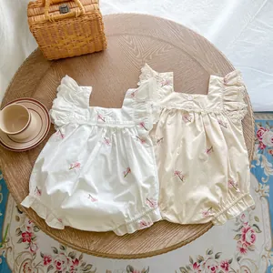 Close-up of white and beige cotton baby rompers with floral embroidery and lace trim