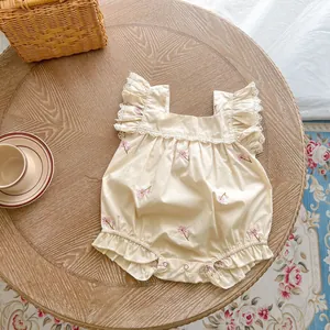 Close-up of cotton baby bodysuit with floral embroidery, lace trim, and metal snap buttons