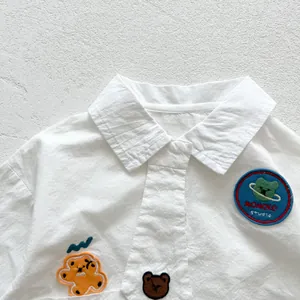 Détail d'une chemise bébé en coton blanc avec broderies de planète et d'ours
