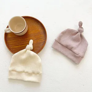 Detail view of baby knitted beanies with ribbed texture and knotted tops in two soft colors