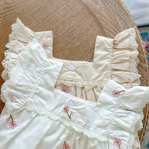 Close-up of baby romper showing square collar with lace trim and pink floral embroidery
