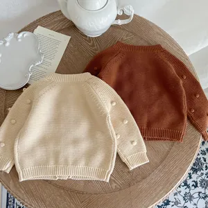 Detail of baby knitted cardigan featuring 3D pom-pom sleeves and ribbed texture