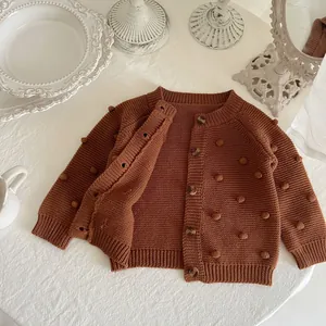 Girl's caramel knit cardigan with handmade pom-poms and buttons in a minimalist flat lay
